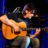 The picture of a guitarist playing on an acoustic guitar sitting on a chair
